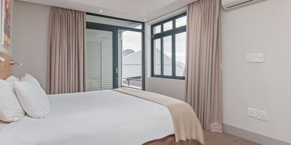 Habitación de hotel con cama, puerta corredera a un balcón y una ventana con cortinas.