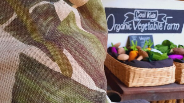 A close-up of a camouflage fabric and a sign for "Cool Kids Organic Vegetable Farm" with baskets of vegetables.