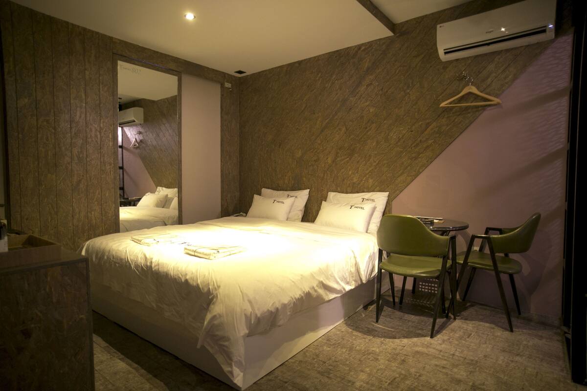 Una habitación de hotel moderna con una cama grande, una mesita, dos sillas y un espejo en la pared.