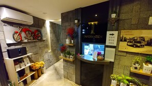 Un área de recepción con una bicicleta colgada, un panel informativo digital y plantas en macetas.