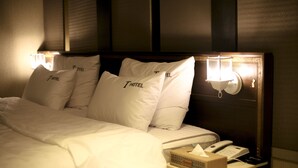 Habitación de hotel con una cama bien hecha, almohadas con el nombre del hotel, lámparas de noche, un teléfono y una caja de pañuelos sobre la mesita de noche.