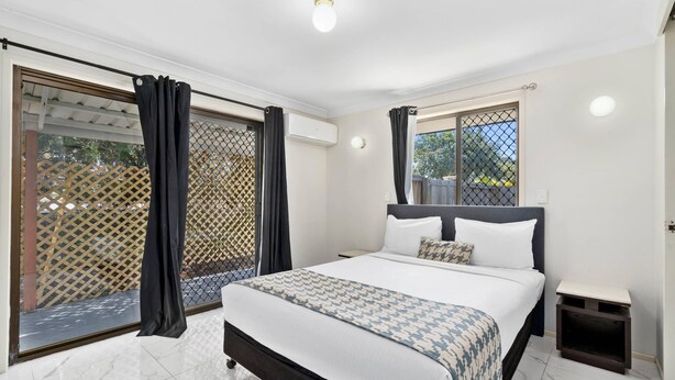 Un dormitorio con cama, mesita de noche, ventana con cortinas y vistas al exterior.
