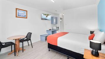 A modern hotel room with a bed, a desk, a chair, a small table, a TV, and a microwave.