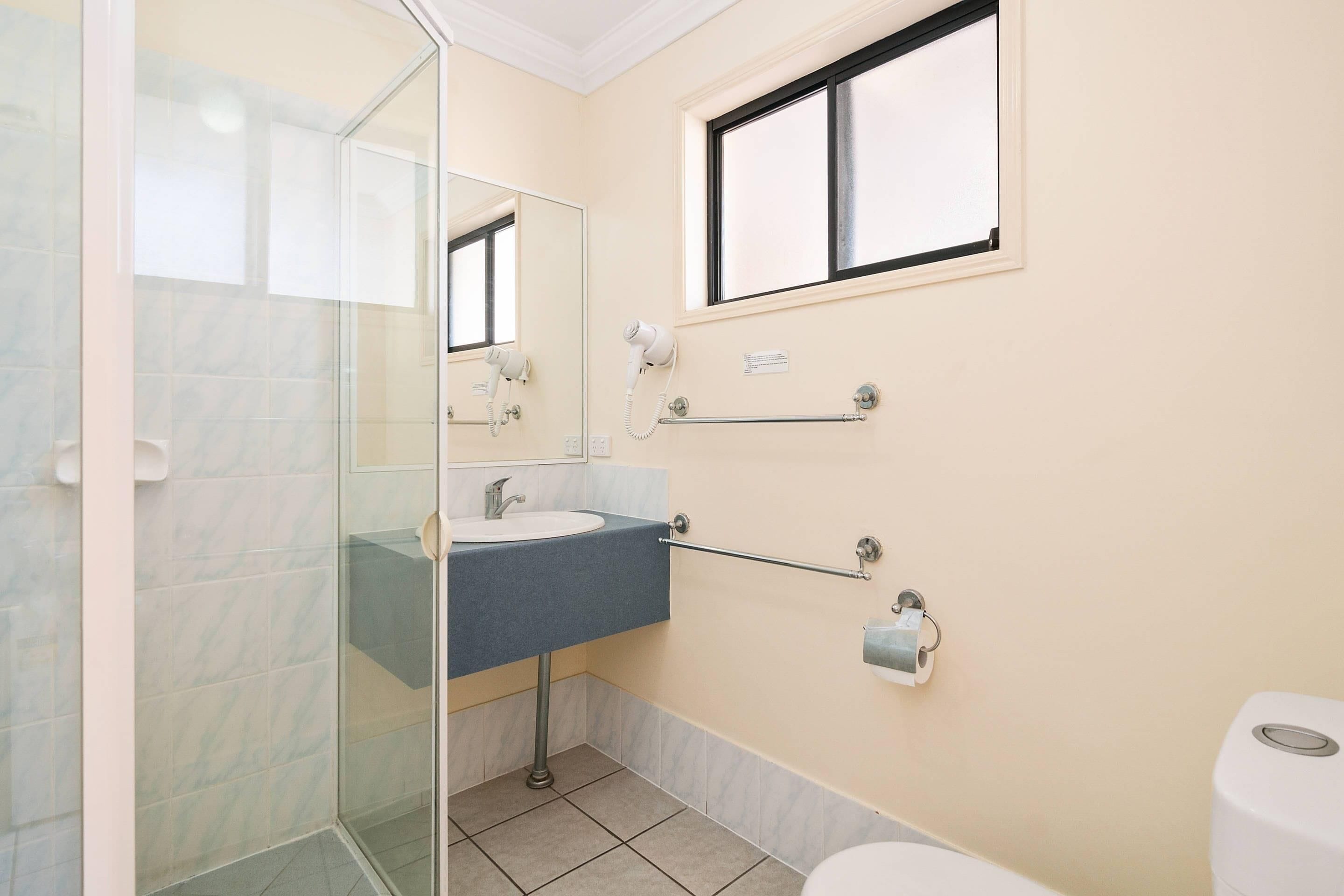 Une salle de bain avec une douche à parois de verre, un lavabo avec un porte-serviettes, des toilettes et une fenêtre.