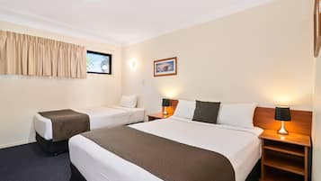 A hotel room with two beds, a window with curtains, a nightstand with a lamp, and a framed picture on the wall.