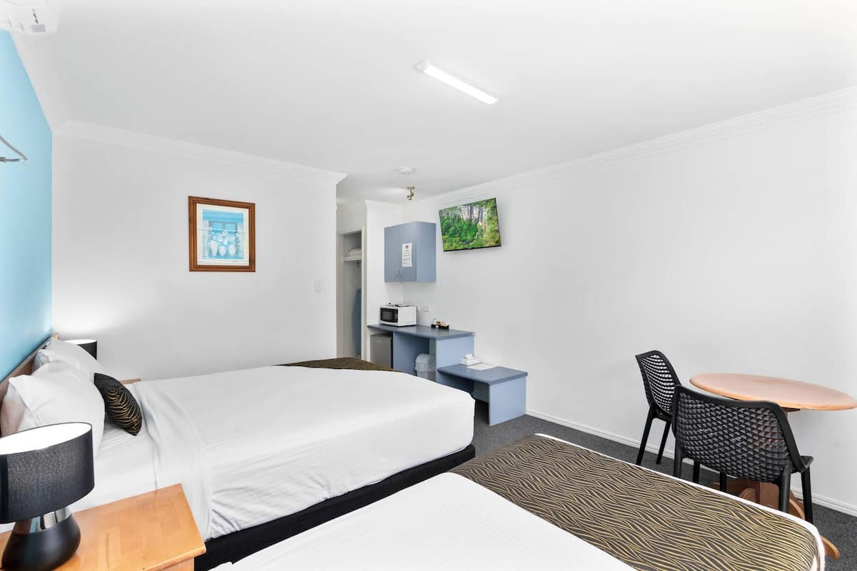 A hotel room with a bed, a desk with a computer, a chair, a small table, and a TV.