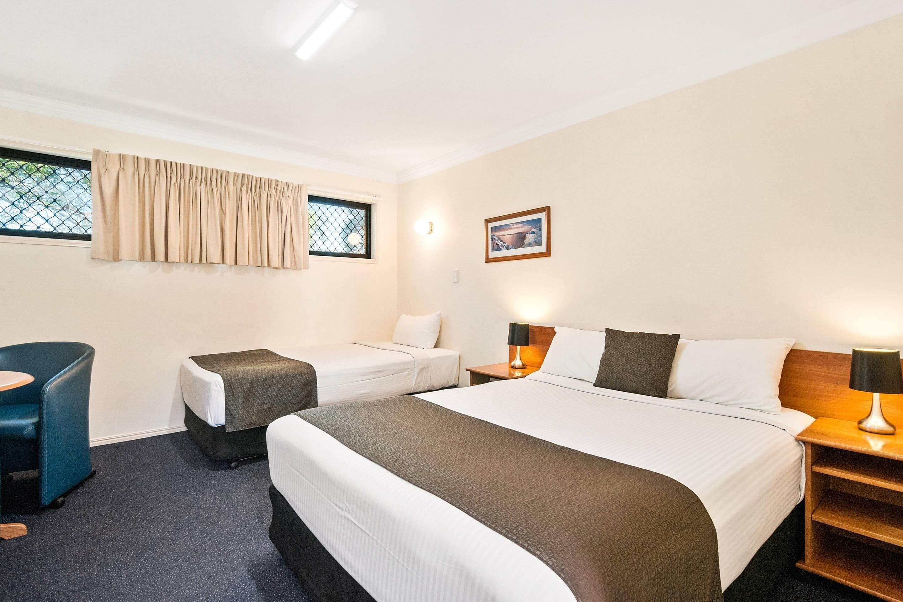 Een hotelkamer met twee bedden, een bureau, een stoel, een raam met gordijnen, een aan de muur hangend schilderij en bedlampjes.