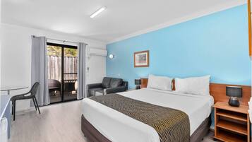 A hotel room with a bed, a desk, a chair, a nightstand, and a view of the outside.