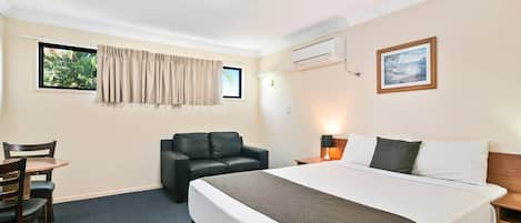 Habitación de hotel con cama, escritorio con sillas, sofá de cuero, ventana con cortinas, equipo de aire acondicionado y un cuadro en la pared.