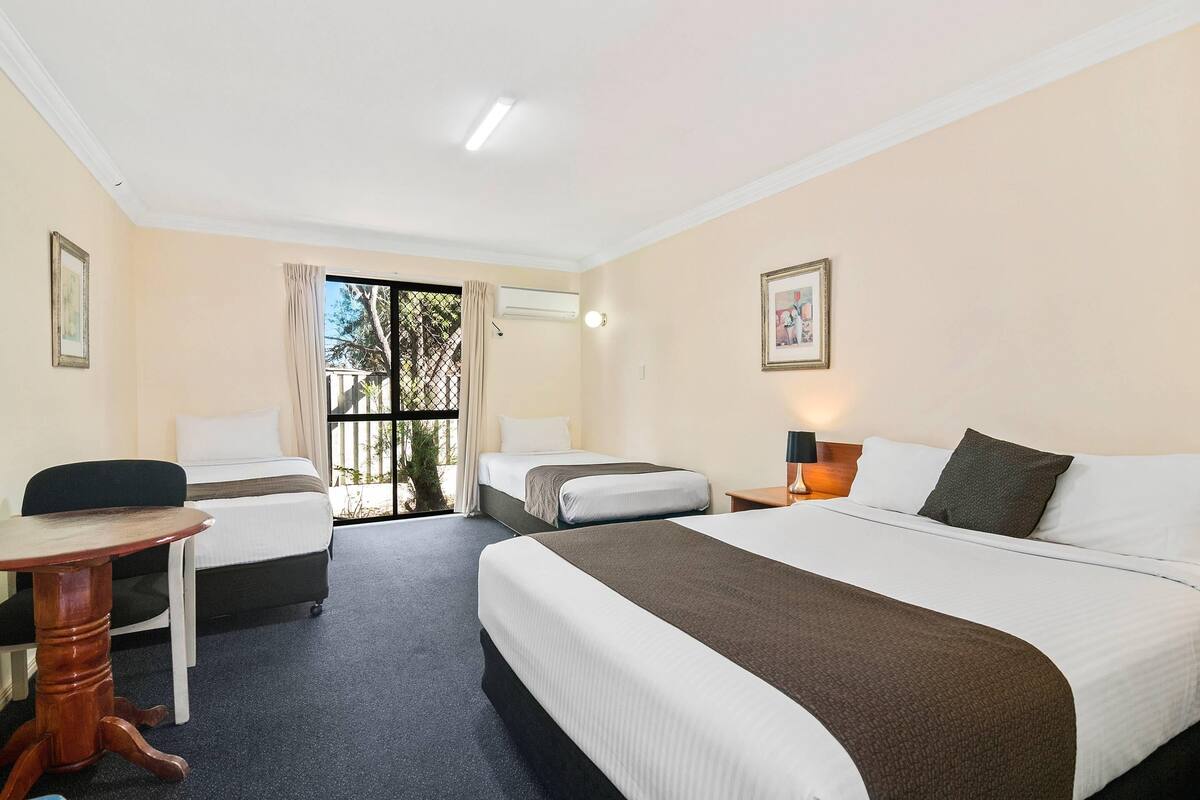A hotel room with two beds, a desk, a chair, and a view through a glass door.