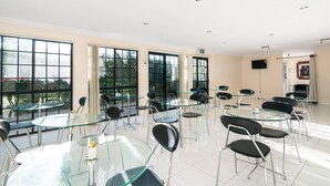 Un salón de conferencias con mesas y sillas de vidrio, ventanas amplias y señal de salida.