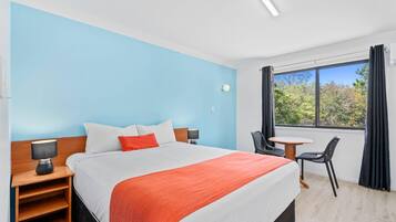 A hotel room with a bed, bedside tables, a chair, a small table, and a window with curtains.