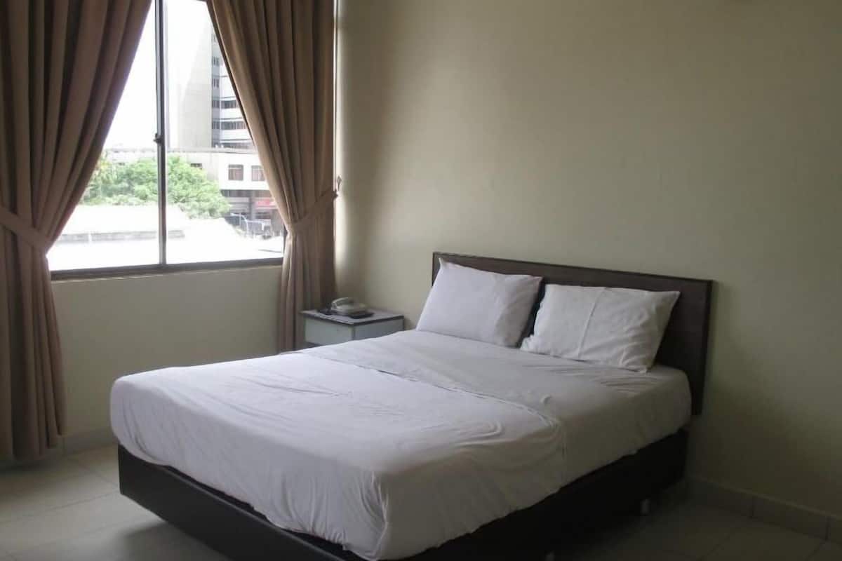 A hotel room with a bed, curtains, a nightstand, and a window with a view of buildings.