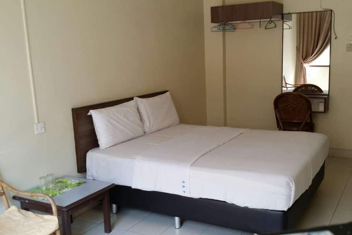 A single bed with a wooden headboard, a small table with a green mat, a chair, and a mirror on the wall.