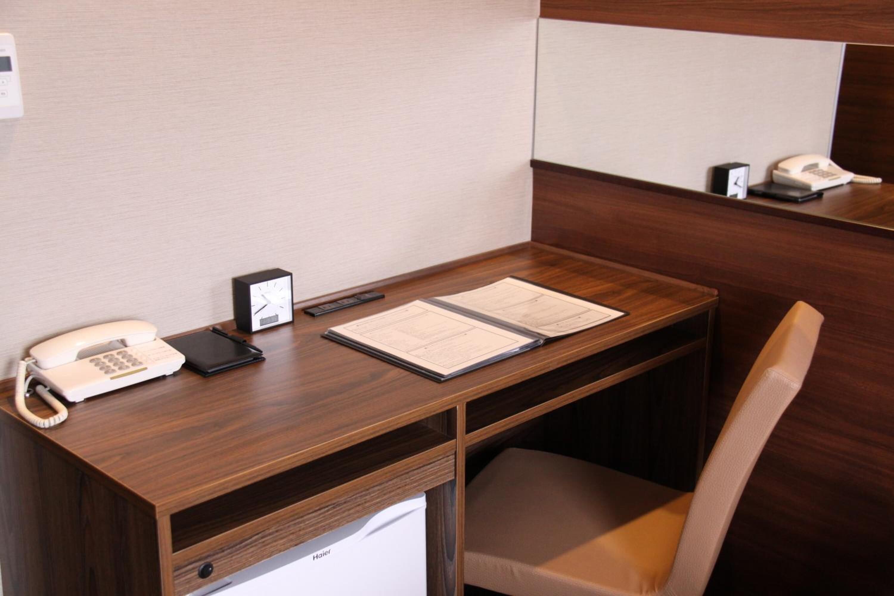 A hotel office cubicle with a wooden desk, a telephone, a notepad, and a chair.