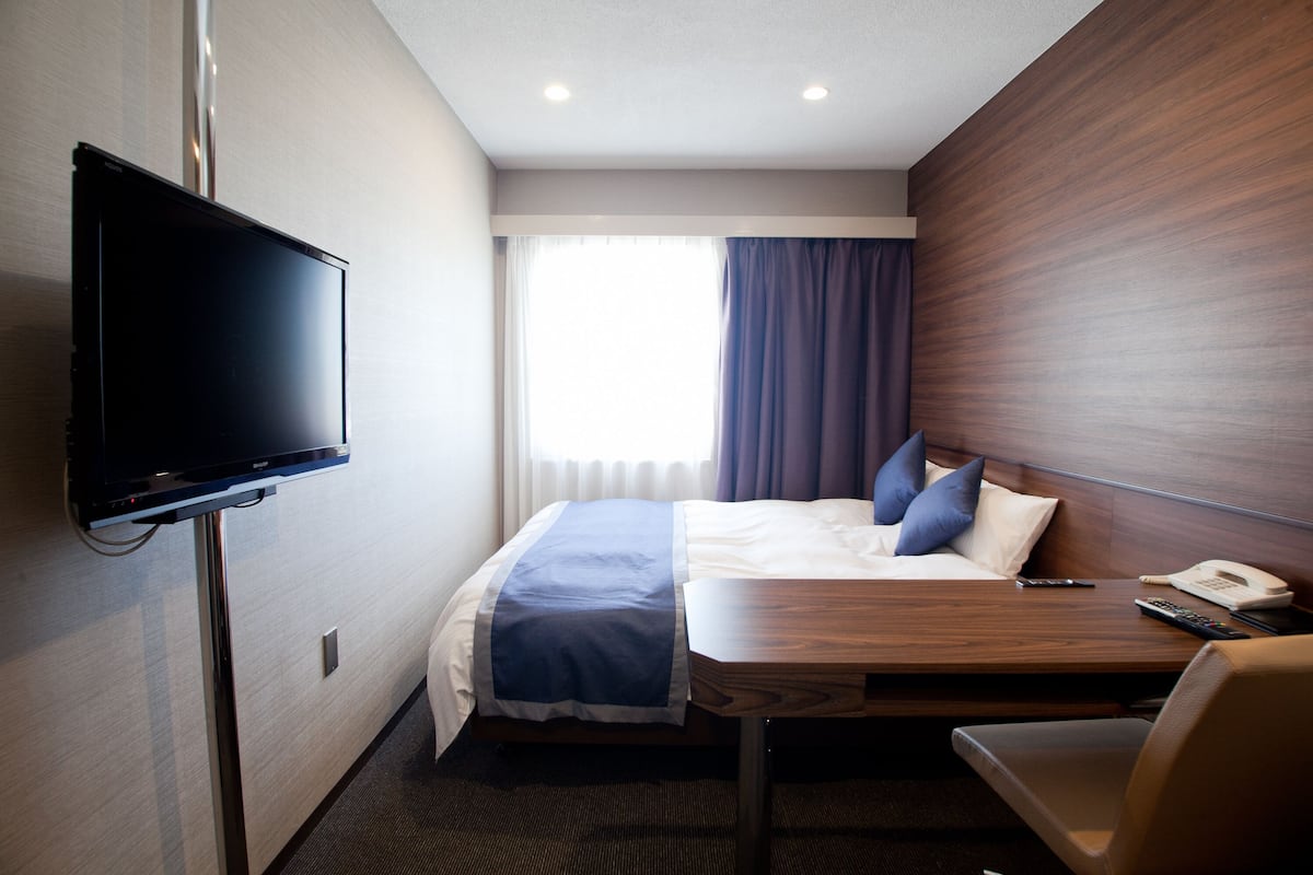 Une chambre d’hôtel équipée d’un lit, d’un bureau, d’une chaise, d’une télévision et d’une fenêtre avec des rideaux.