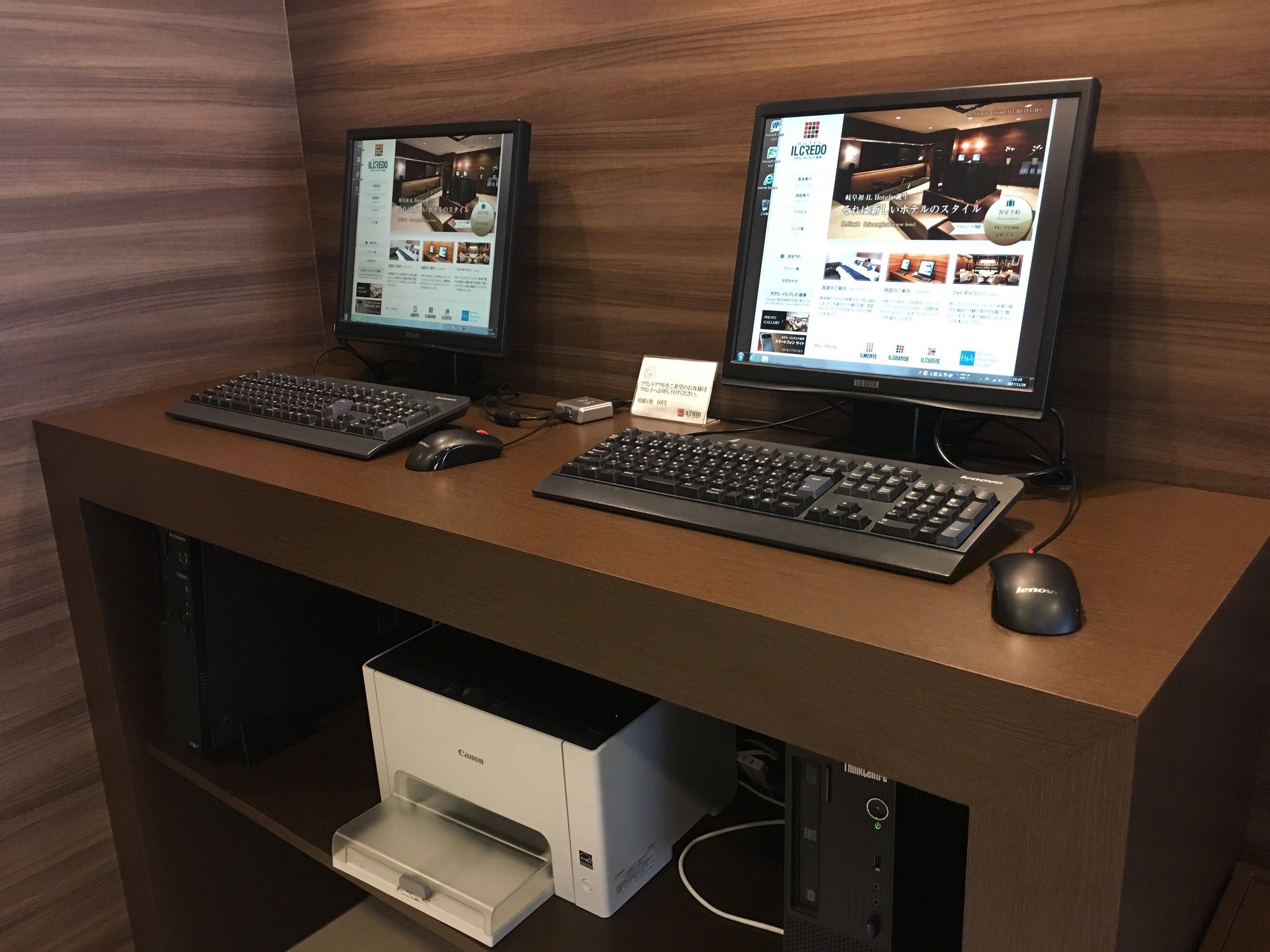 A dual-monitor setup on a wooden desk with two keyboards and a mouse.