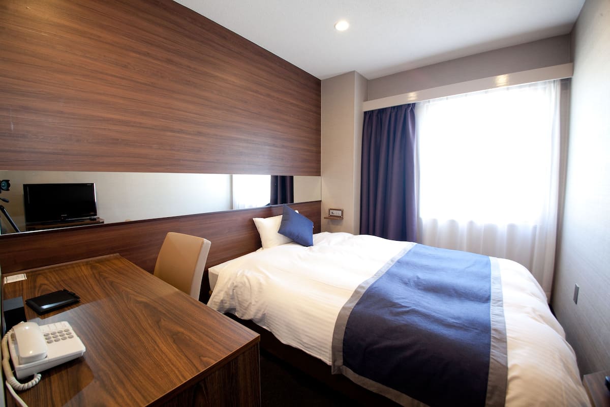 Une chambre d’hôtel avec une tête de lit en bois, un lit avec une literie blanche et bleue, un bureau avec un téléphone et un téléviseur fixé au mur.