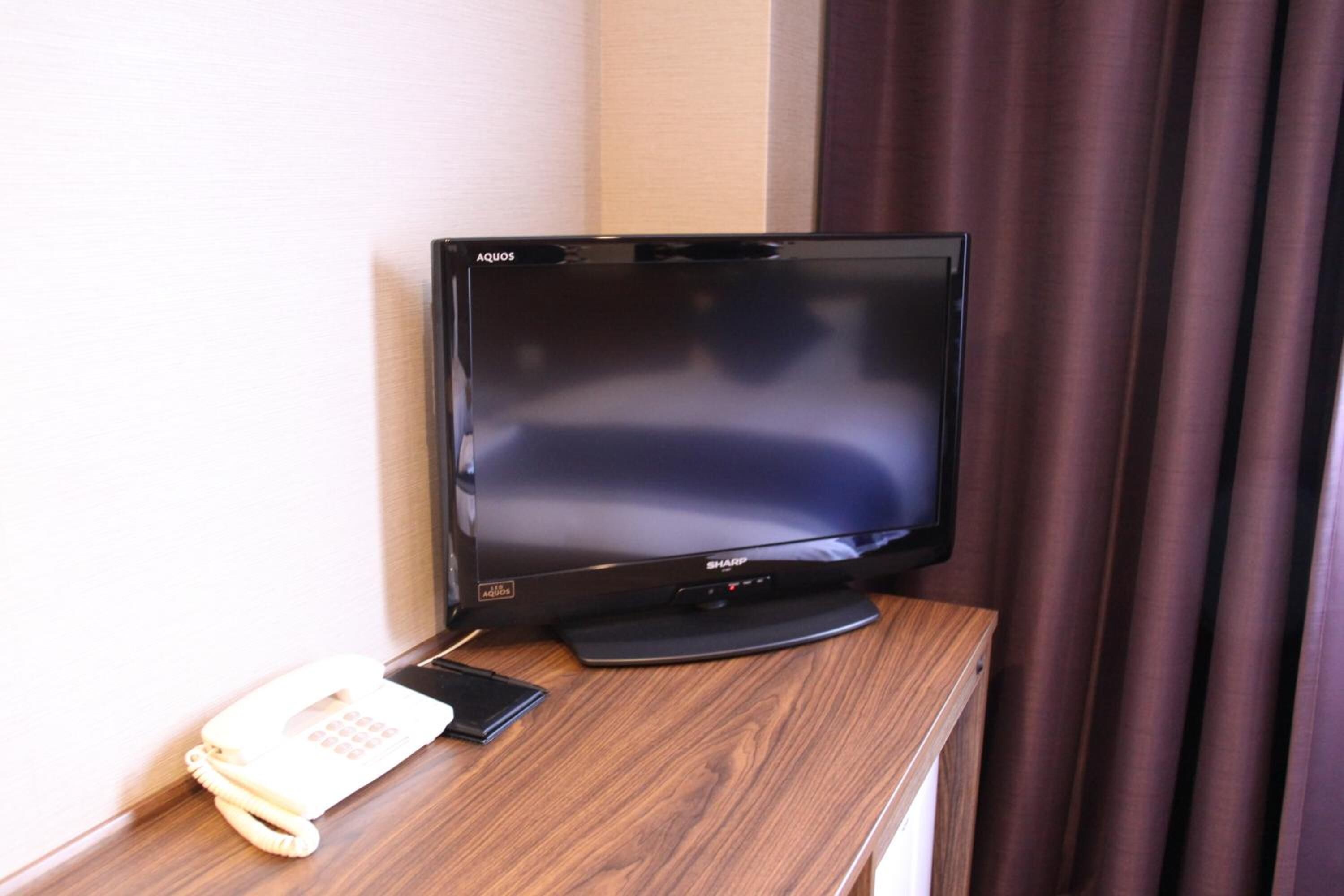 Ein flachbildfernseher von Sharp auf einem Holztisch, zusammen mit einem weißen Telefon.