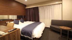 Habitación de hotel con cama, sofá, una pequeña mesa redonda y un escritorio con teléfono y control remoto.