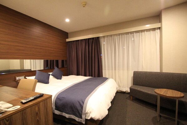 Habitación de hotel con cama, sofá, una pequeña mesa redonda y un escritorio con teléfono y control remoto.