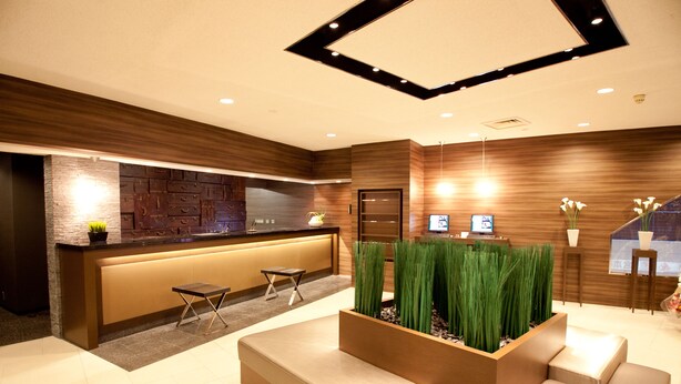 Una moderna zona de recepción con un mostrador de madera, asientos y plantas decorativas.