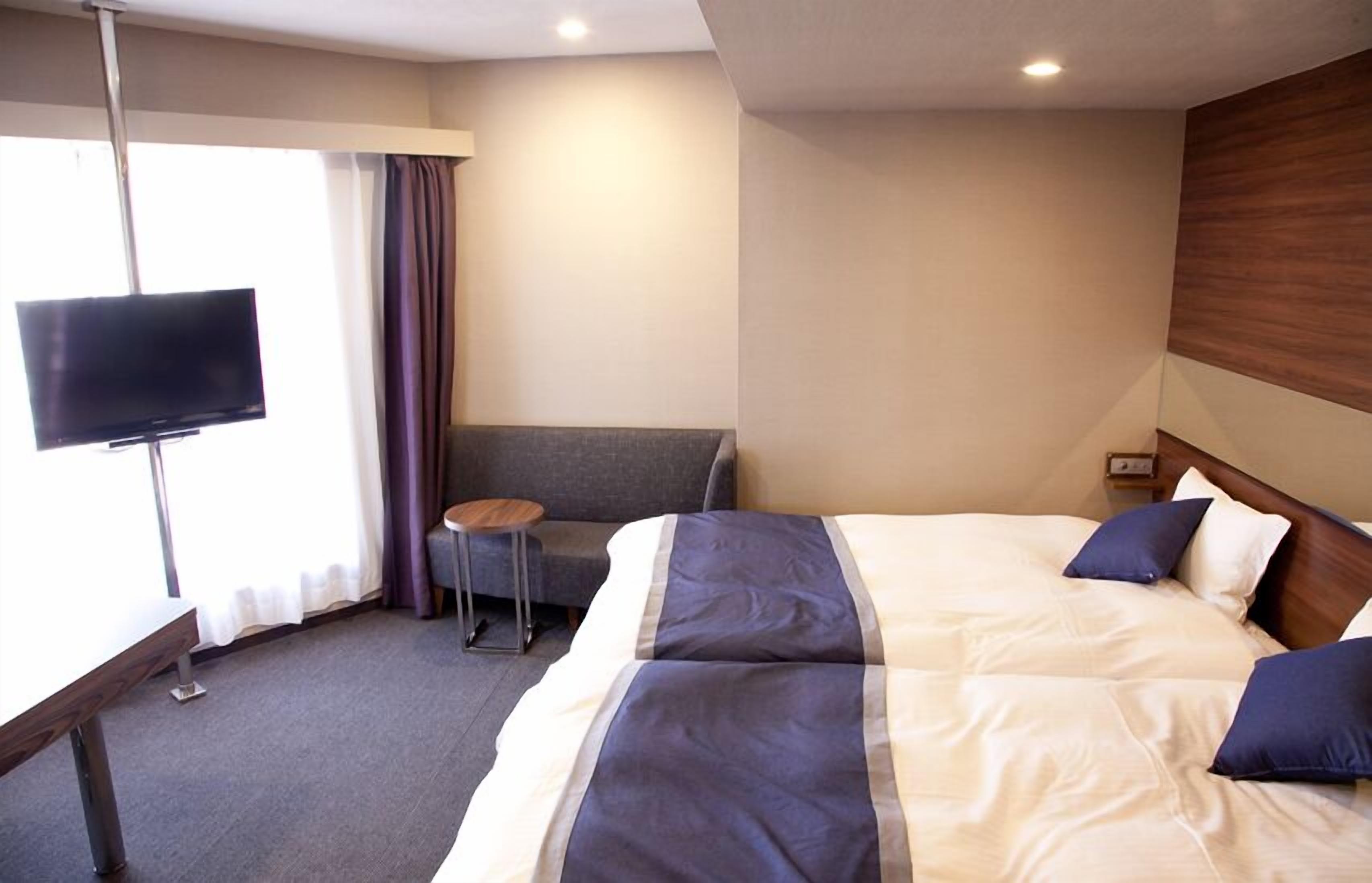 Habitación de hotel con una cama grande, un televisor montado en la pared, una mesita pequeña y un sofá.