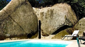 Une piscine bordée de gros rochers et d’un mur de pierre, entourée de chaises longues.