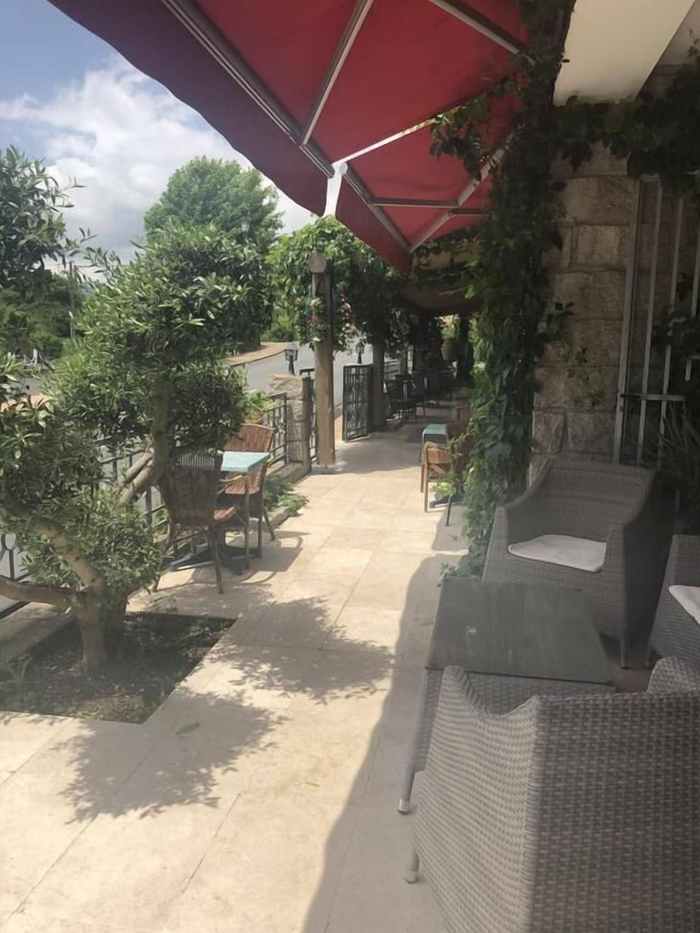 Un espace extérieur aménagé en terrasse, avec des meubles en osier, un parasol rouge et de la verdure.