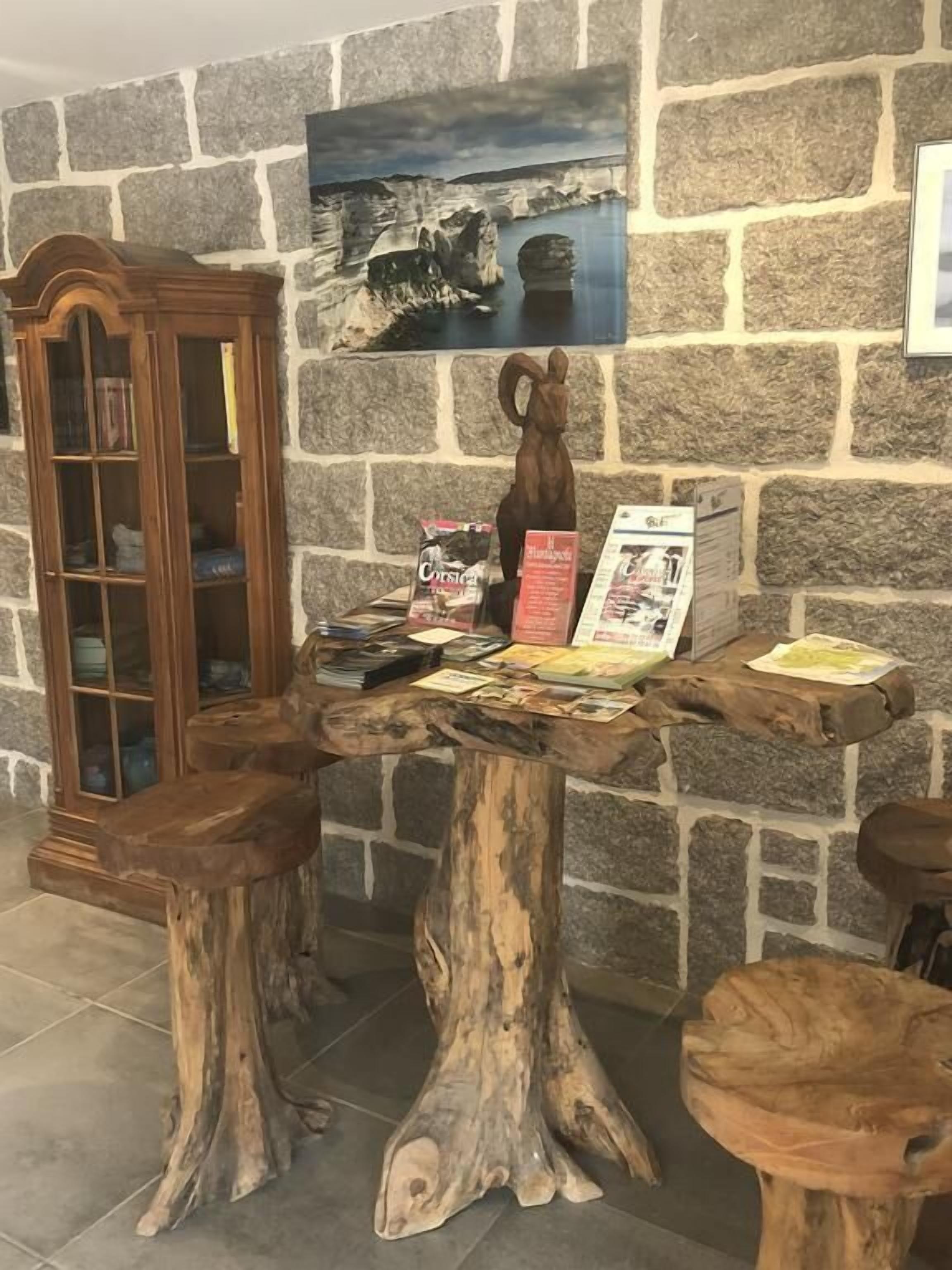 A rustic wooden table with a carved wooden stool, a wooden cabinet, and a framed picture on a stone wall.