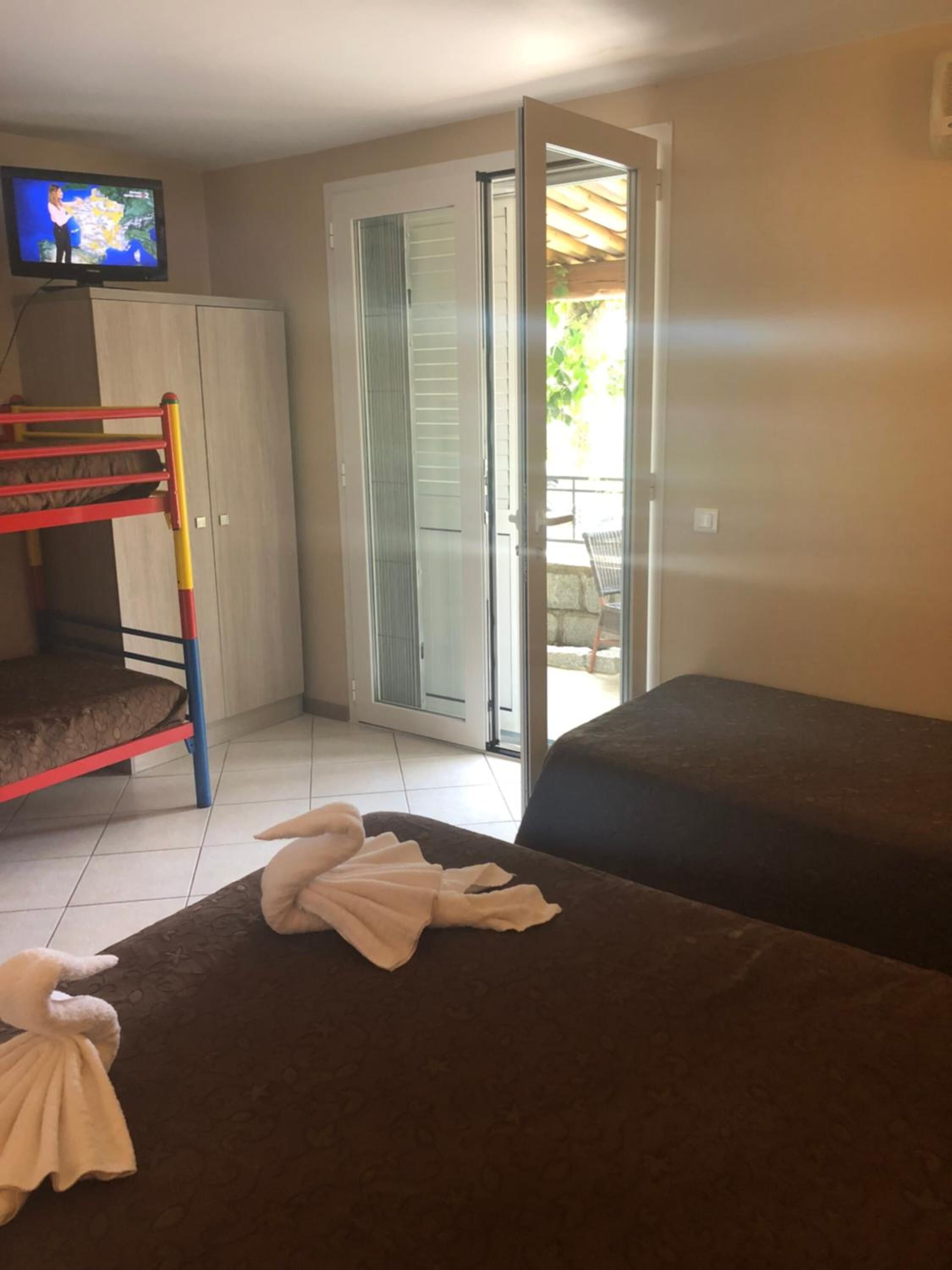 A room with a bunk bed, a sofa, a television, and a sliding glass door leading to an outdoor area.