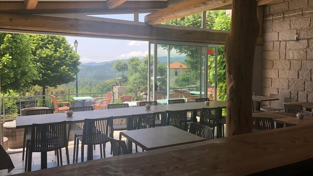 Un espace extérieur aménagé pour les repas, avec des tables et des chaises, de grandes fenêtres offrant une vue sur la verdure et les bâtiments situés au loin.