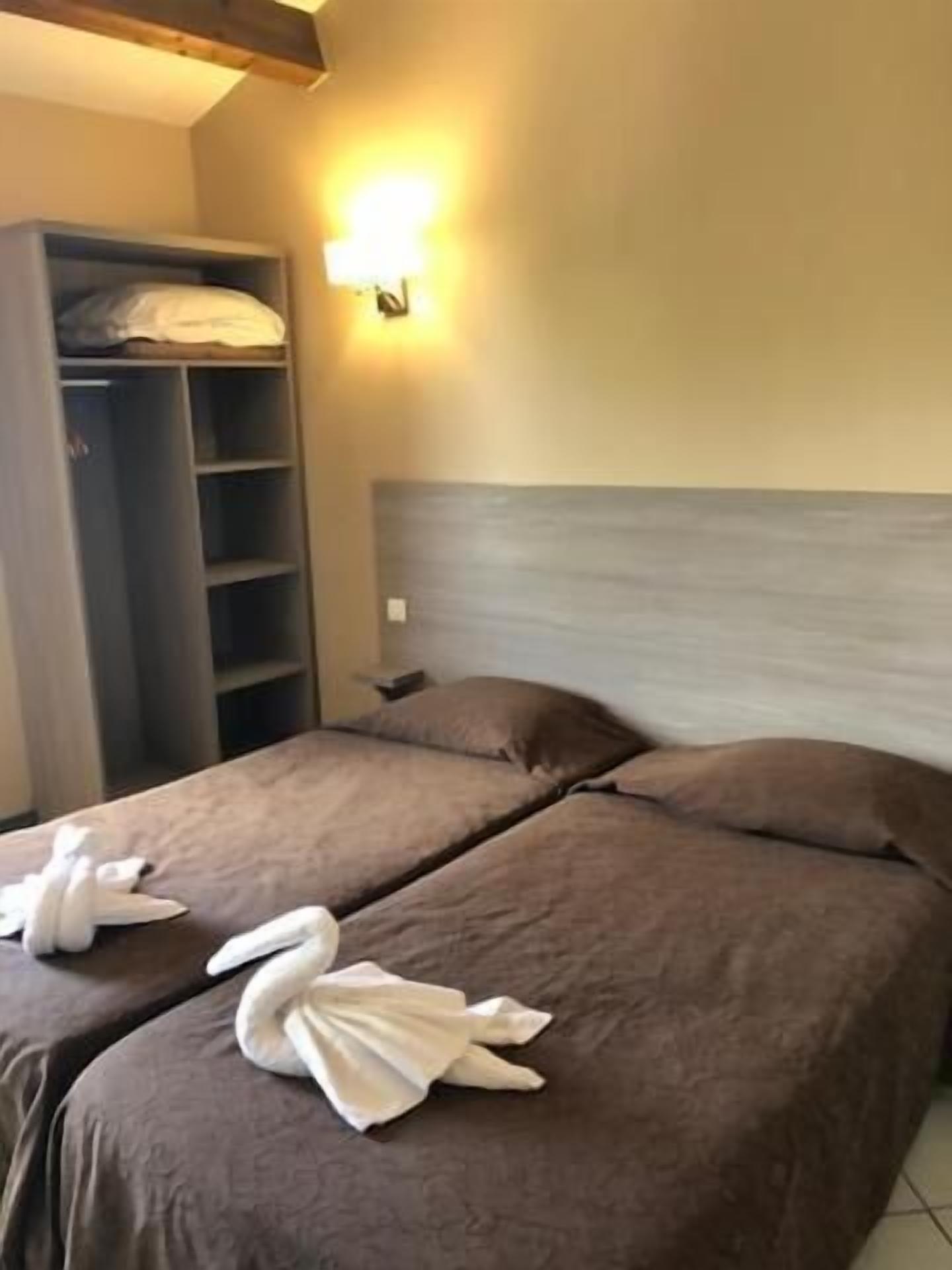 Habitación de hotel con dos camas, un armario y una lámpara fijada a la pared.