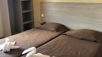 Habitación de hotel con dos camas, un armario y una lámpara fijada a la pared.