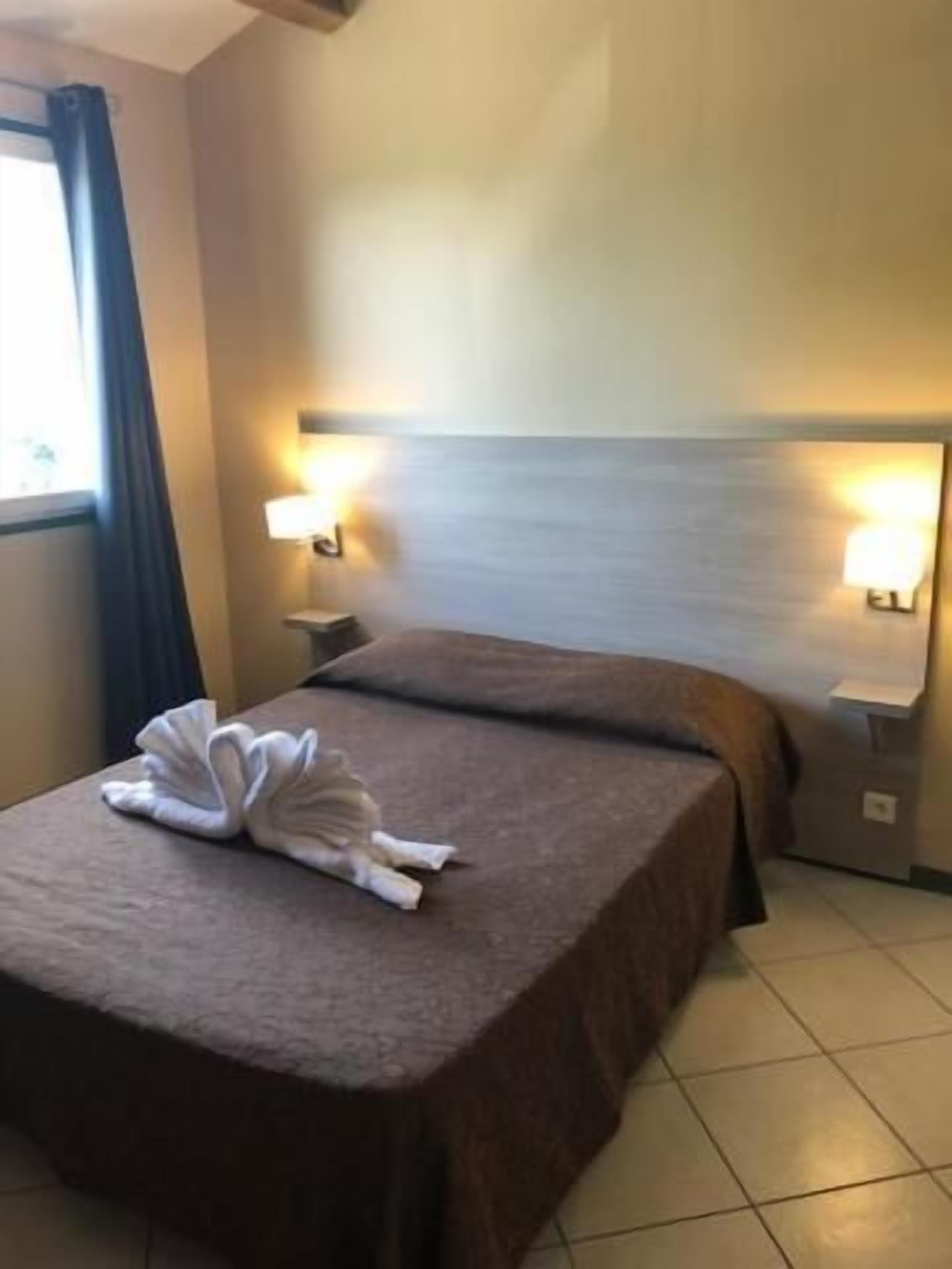 A hotel room with a bed, two bedside lamps, and a window with curtains.