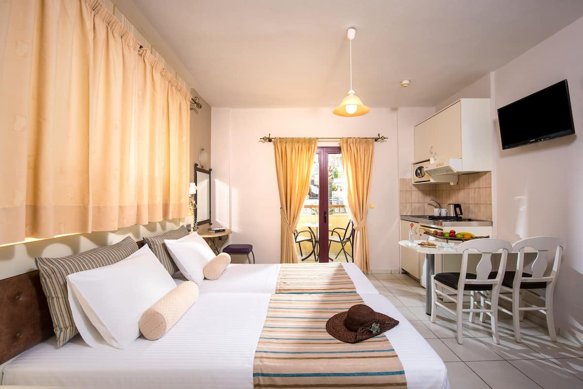 A hotel room with a bed, a desk, a chair, a TV, and a balcony with curtains.
