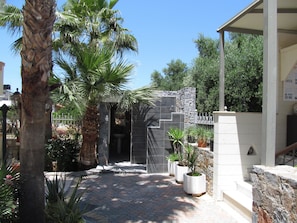 A courtyard with a stone wall, palm trees, and potted plants. - Bella Elena (Hersonissos)