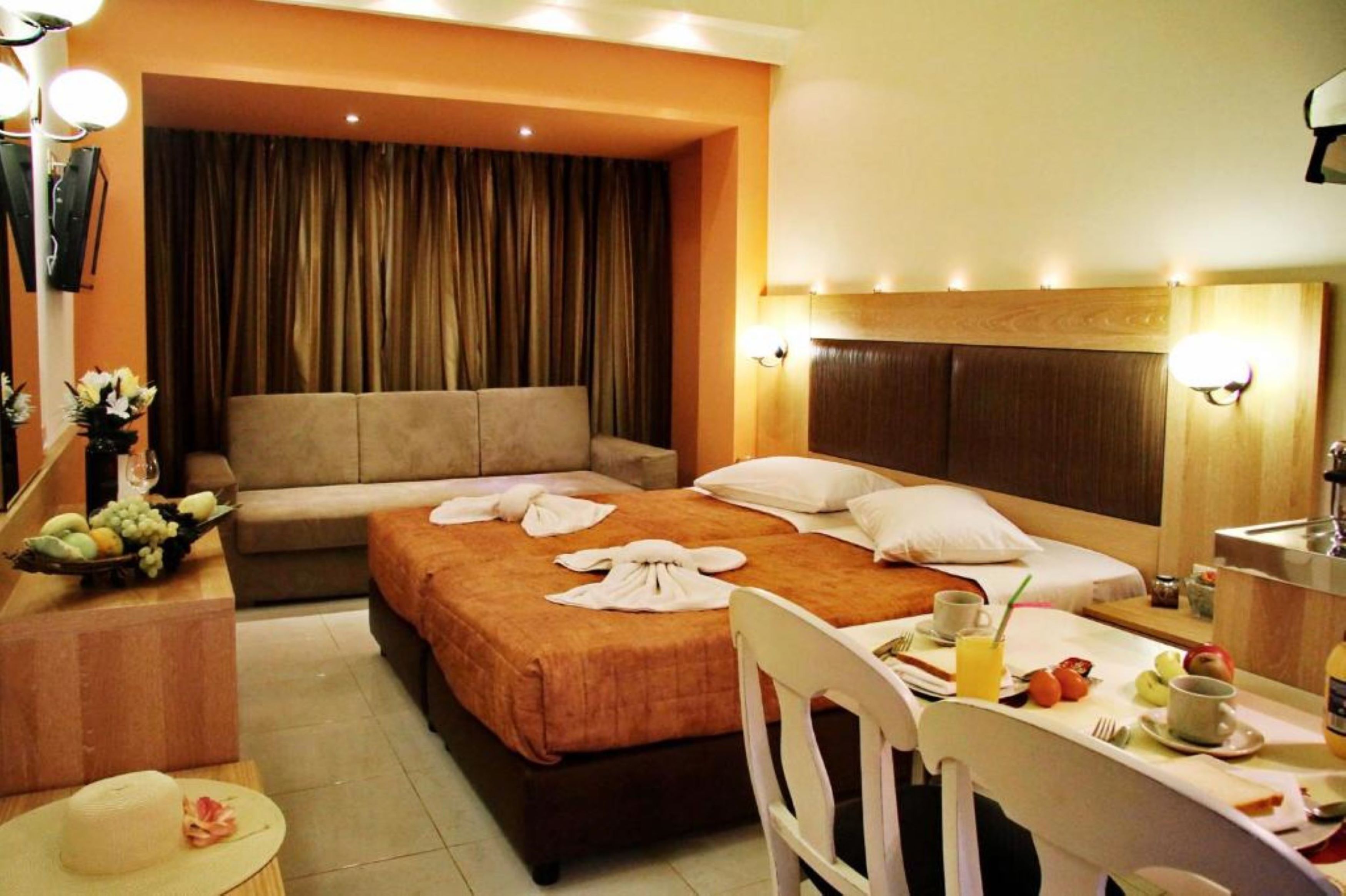 A hotel room with a bed, a sofa, a dining table with breakfast items, and a bathroom area.