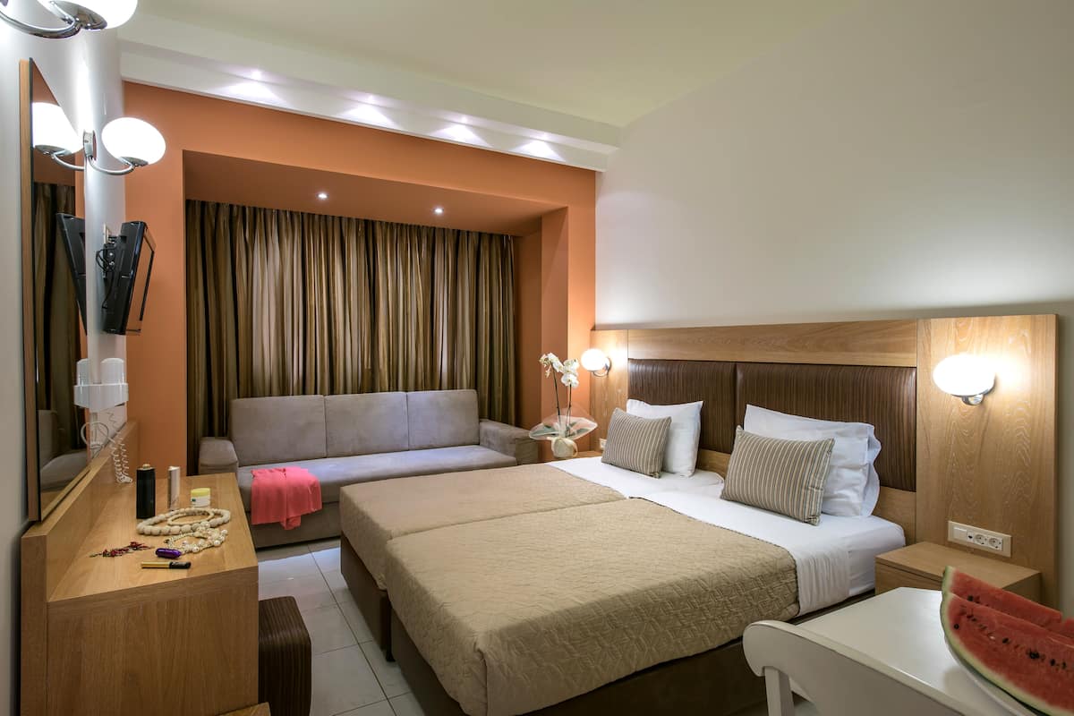 A hotel room with two beds, a sofa, a desk with a mirror, and a nightstand with a lamp.