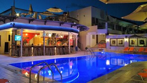 Una zona de bar con taburetes, una piscina con borde iluminado en azul y una escalera que lleva a un nivel superior.