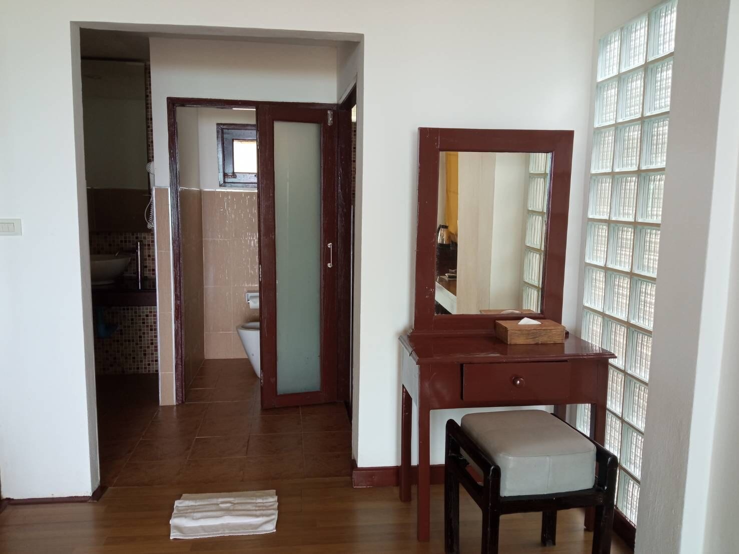 Un couloir avec un plancher en bois, un miroir posé sur une commode en bois, et une salle de bain carrelée visible à travers une porte ouverte.