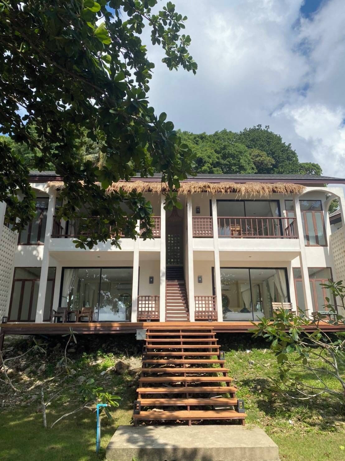 A two-story building with a thatched roof, large windows, and a staircase leading to the upper floor.