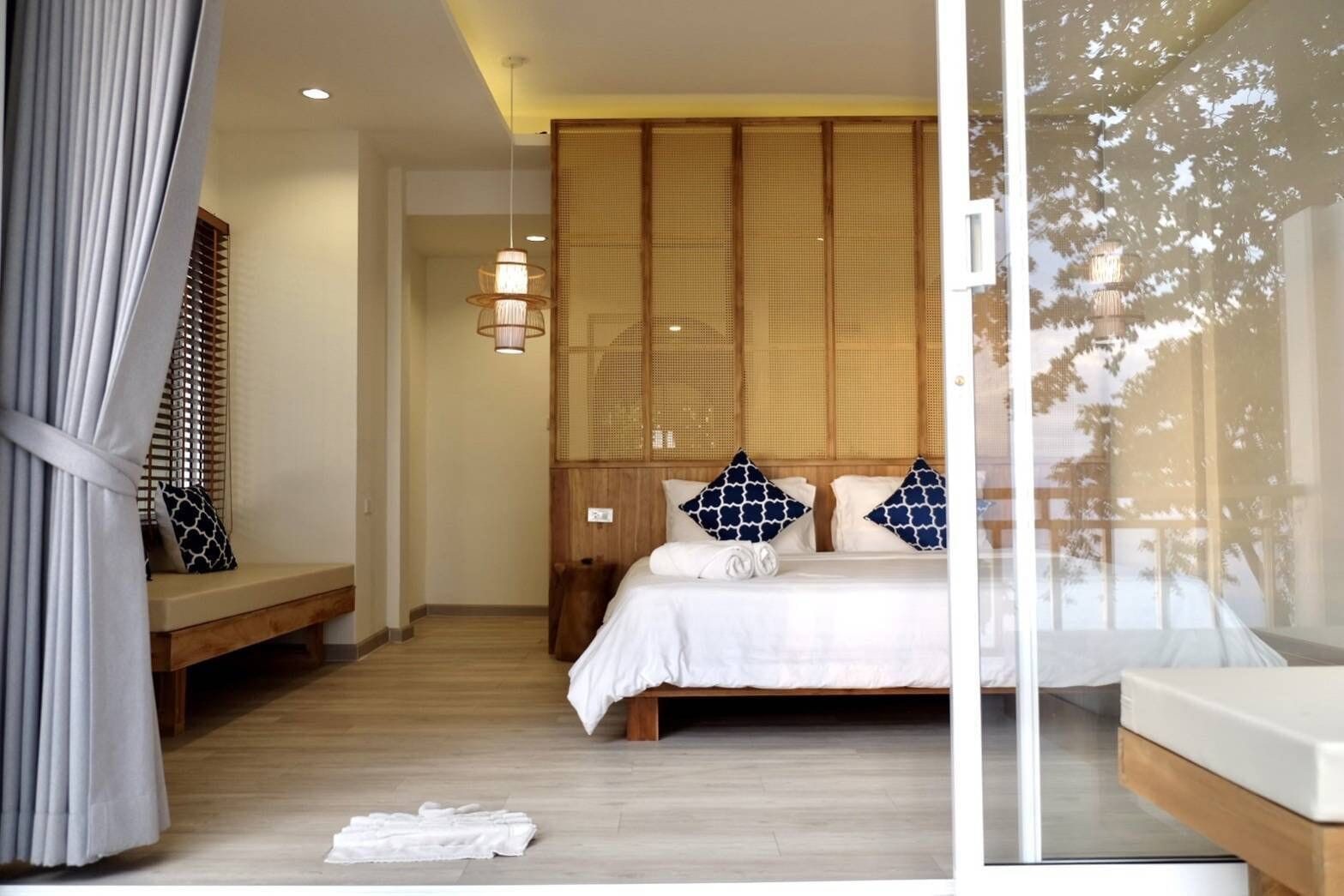 A bedroom with a bed, a bench, a hanging light, and a view of trees through a window.