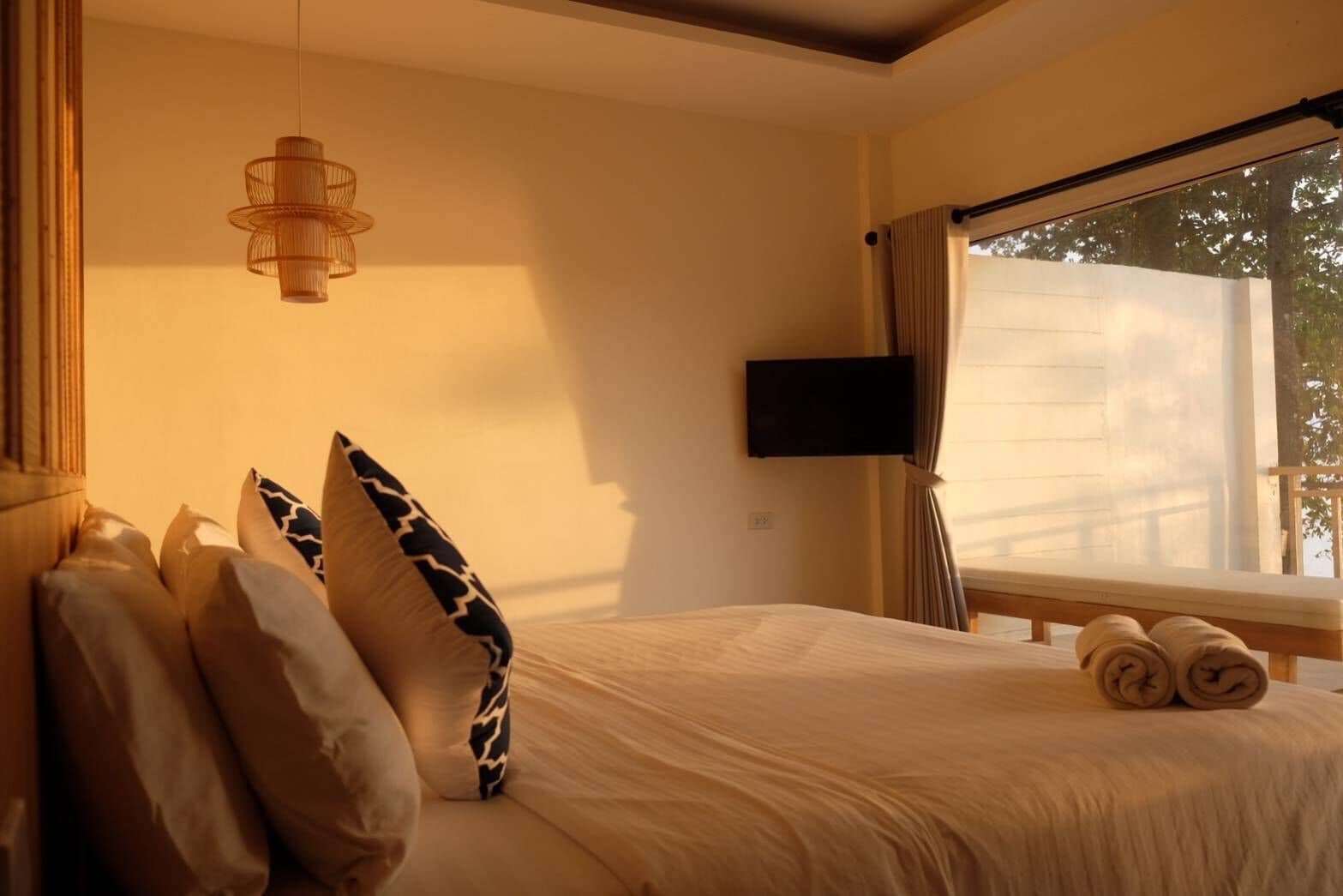 A bedroom with a bed, pillows, a TV, and a window with curtains.