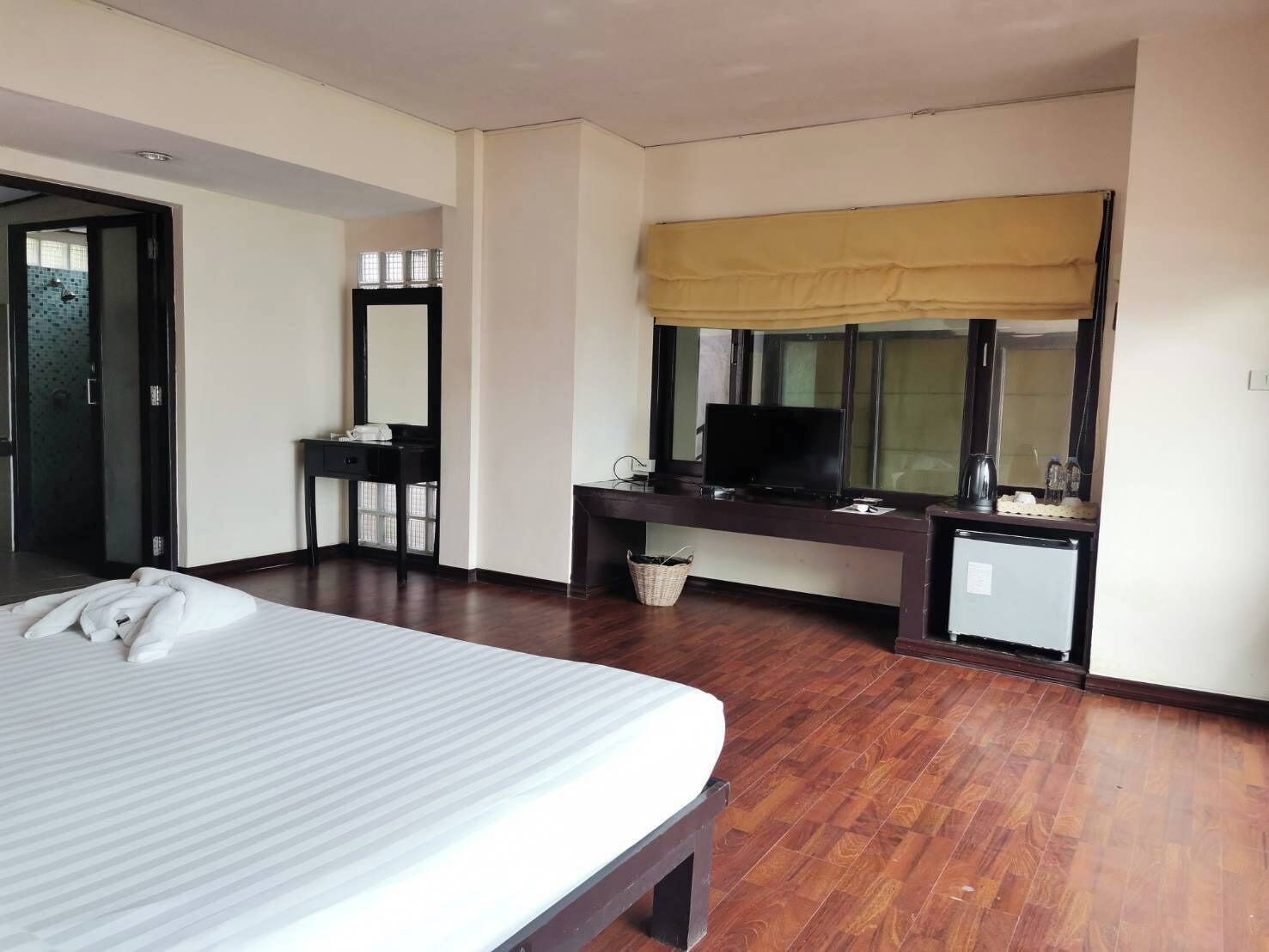 A hotel room with a large bed, a desk with a television, a small refrigerator, and a window with a yellow blind.