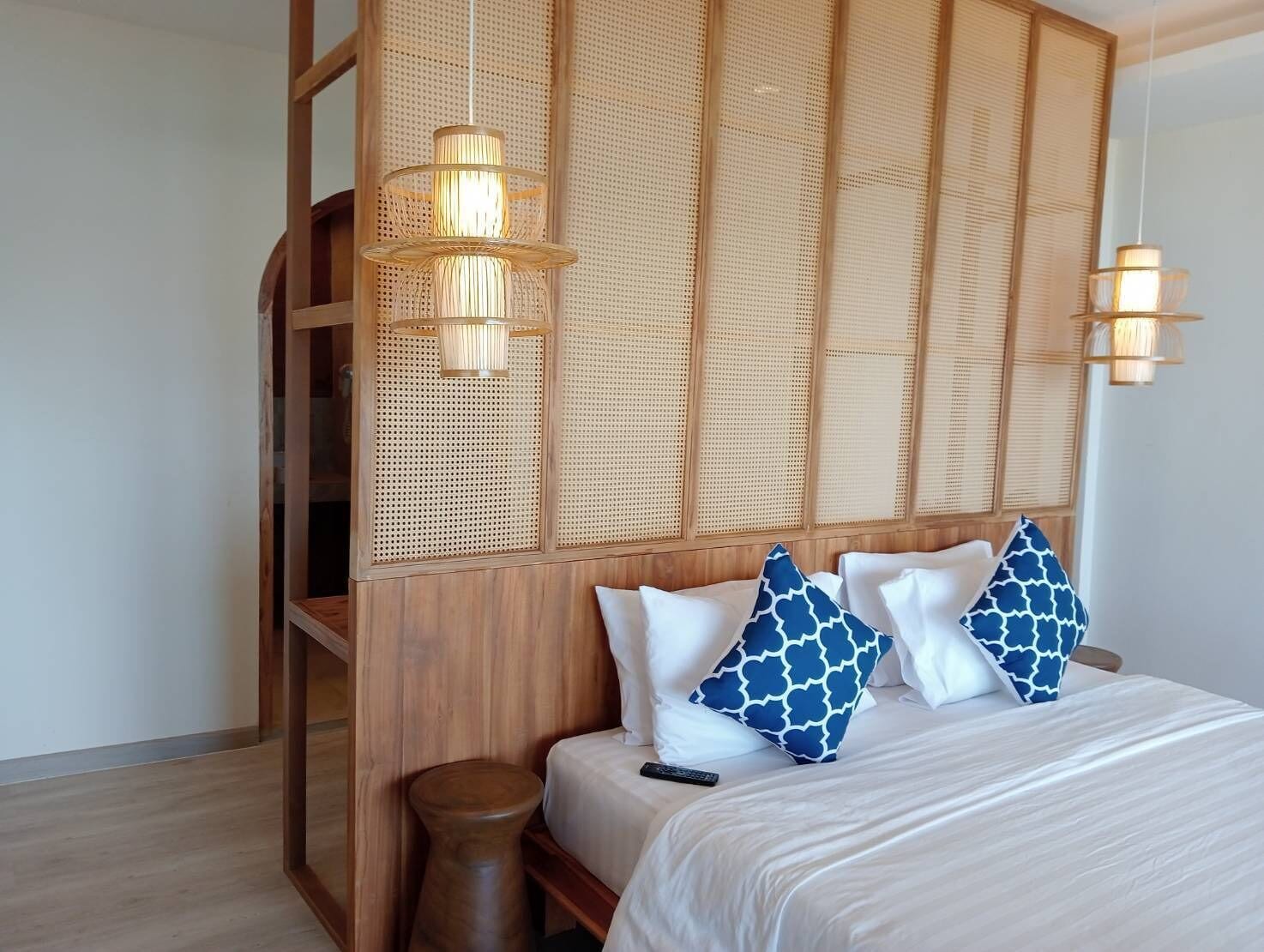 A bedroom with a wooden headboard, a bed with white bedding and blue patterned pillows, a wooden nightstand, and two hanging lamps.