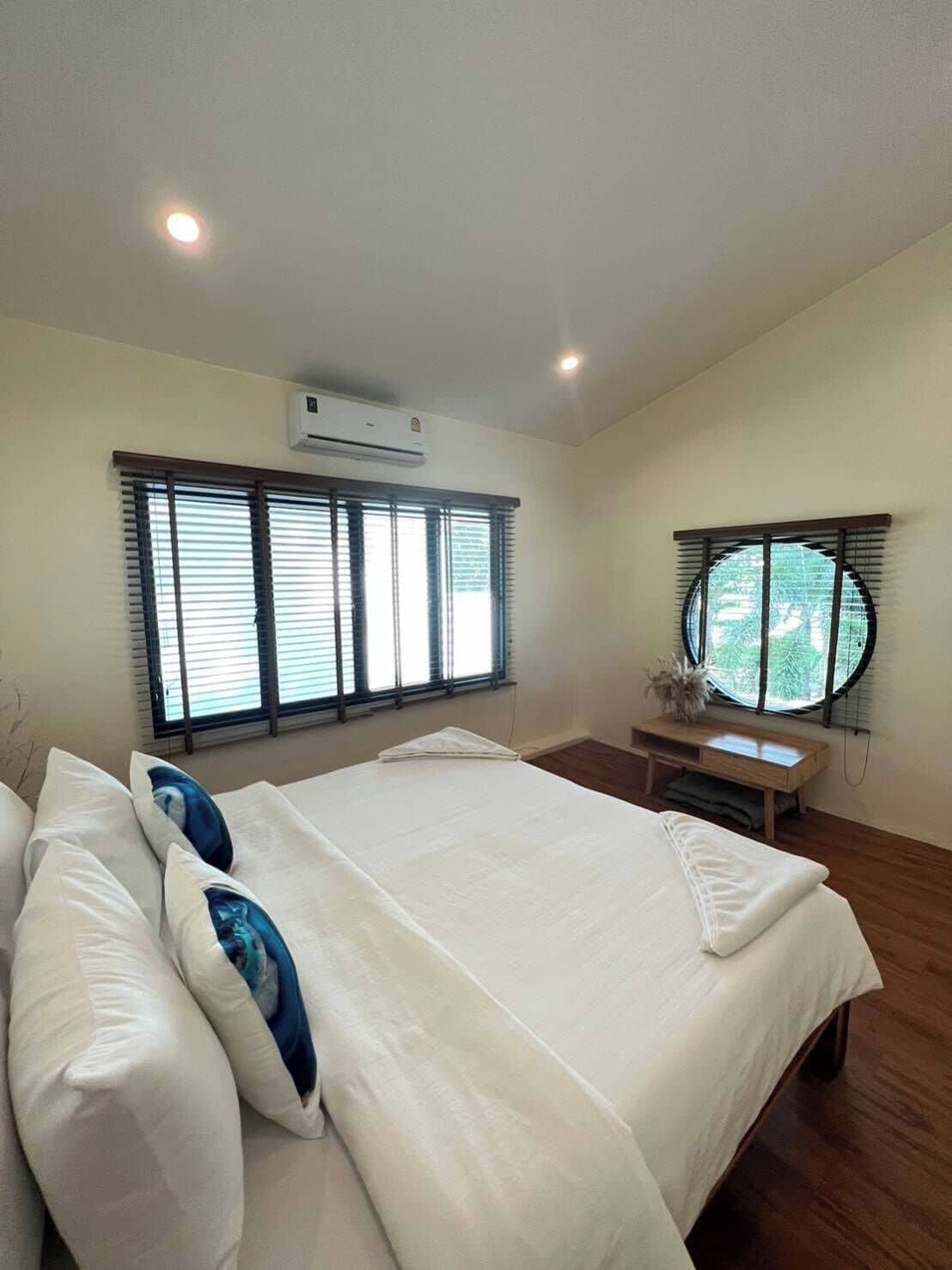 A bedroom with a bed, two windows, a bench, and an air conditioning unit.