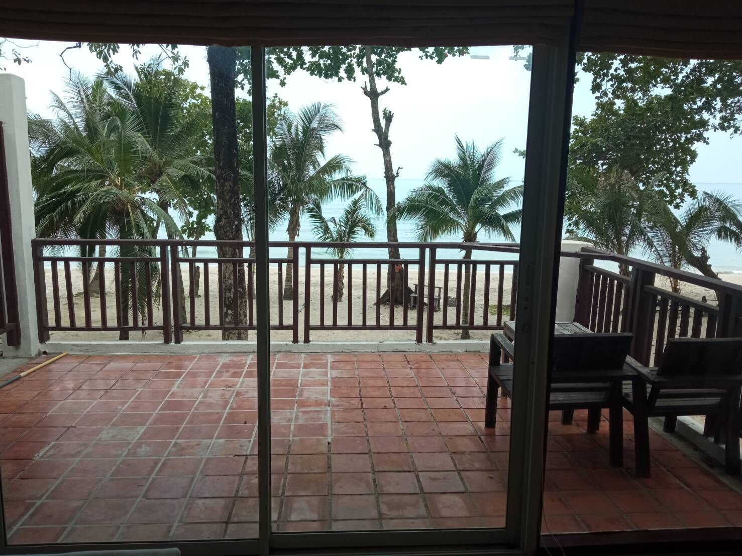 Un patio cubierto con vista a una playa, palmeras y una barandilla de madera.