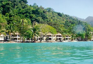 Um resort costeiro com villas na praia, vegetação exuberante e águas turquesa cristalinas.