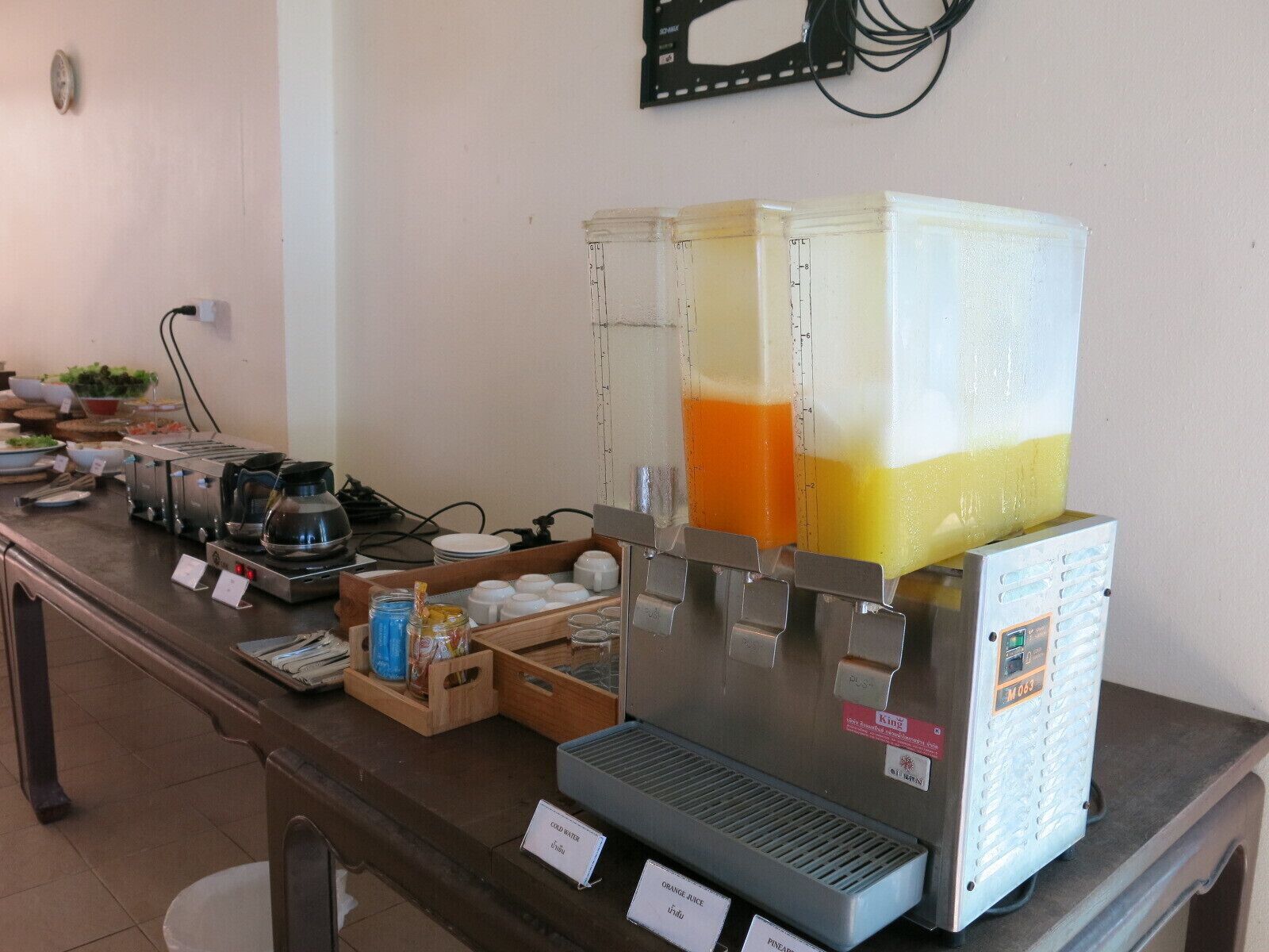 A breakfast bar with a juice dispenser, coffee maker, and various food items.